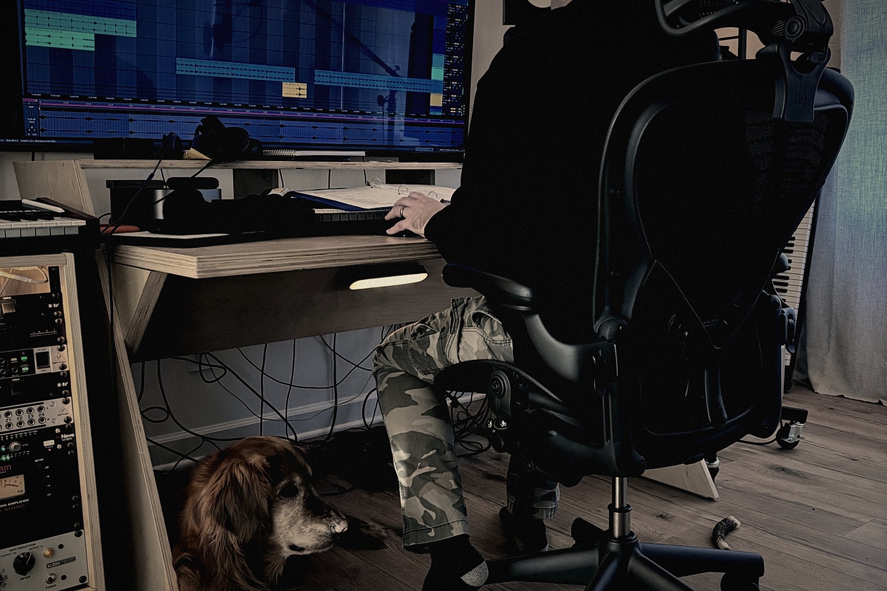 Brock at the studio desk, a session open on the monitor, the dog asleep underneath